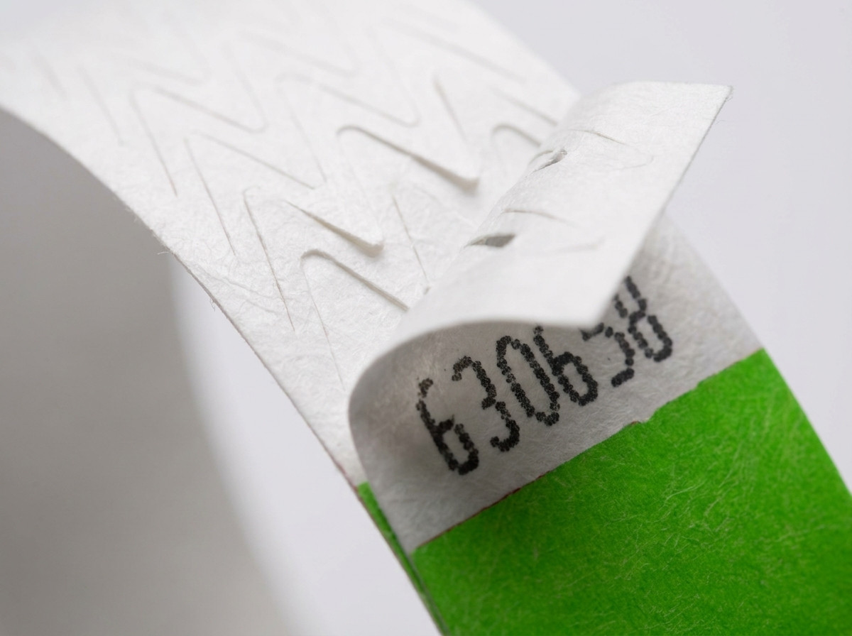 Close-up of the anti-transfer closure of a coloured Tyvek wristband during an access control check at a festival